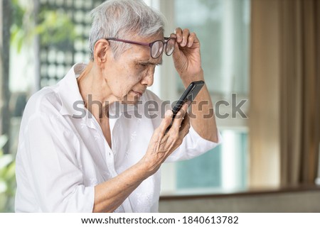 Asian senior woman with eye glasses,try to read messages,gaze at the small text on mobile phone,age related macular degeneration,blurred vision,poor eyesight problems,eye disease of the old elderly