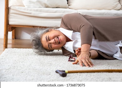 Asian senior woman falling down on carpet and lying on the floor in living room at home, Falls of older adults concept