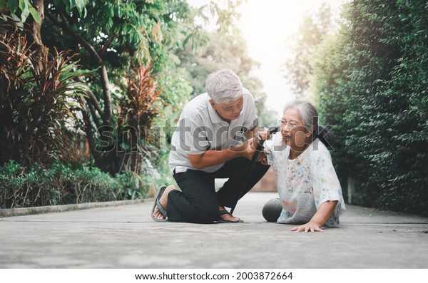 Asian senior woman falling down on lying floor at\
home after Stumbled at the doorstep and Crying in pain and her\
husband came to help support. Concept of old elderly insurance and\
health care