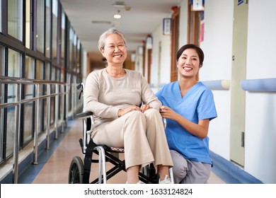 Asian Senior Woman And Her Caregiver Looking At Camera Smiling