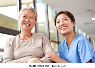 Asian Senior Woman And Her Caregiver Looking At Camera Smiling