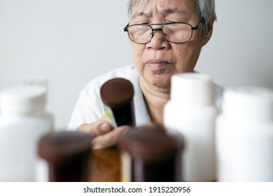 Asian Senior Woman Holding Drug Bottle In Front Of Medicine Cabinet In Her Home,reading The Label On A Bottle For Medical Treatment,old Elderly Checking Expiration Date Or Deterioration Of Medication