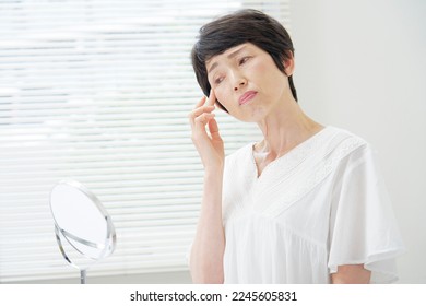 Asian senior woman looking in the mirror at home - Shutterstock ID 2245605831