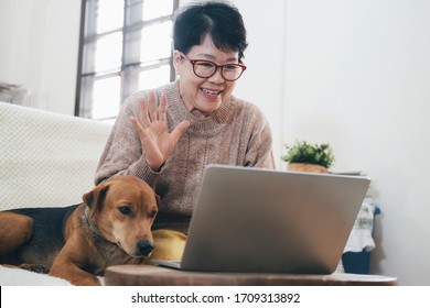 Asian senior woman making video call on laptop , waving at screen, chatting online with people who distance.