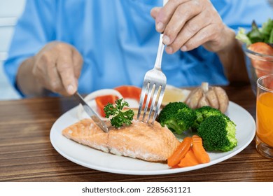 Asian senior woman patient eating Salmon steak breakfast with vegetable healthy food while sitting and hungry on bed in hospital. - Powered by Shutterstock