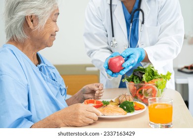 Asian senior woman patient eating Salmon steak breakfast with vegetable healthy food while sitting and hungry on bed in hospital. - Powered by Shutterstock