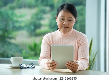 asian senior woman sitting by glasses window and enjoy using tablet internet connection. concept technology in older generation, elderly people with online social media - Powered by Shutterstock