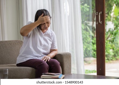 Asian Senior Woman Sitting On Sofa Having Headache At Home. Old Female   Stressed Dizzy . Elderly Touching Her Head With Her Hands While Having Migraine Or Alzheimer .memory Loss . Indoor. Copy Space