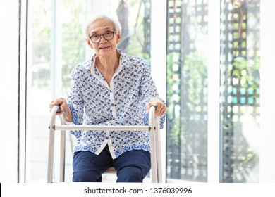 Asian senior woman sitting with walker during rehabilitation, elderly woman wear glasses,smiling and looking at camera in home