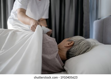 Asian senior woman is sleeping on a bed in bedroom,female caregiver cover senior patient with blanket,assisting old people,putting up the blanket on elderly at nursing home,assistance,care,support