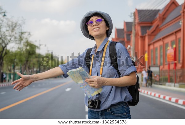  Asian senior woman\
tourist holding a local map and call for car while travelling in\
Bangkok Thailand.