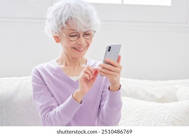 Asian senior woman using the smartphone in the living room - Powered by Shutterstock