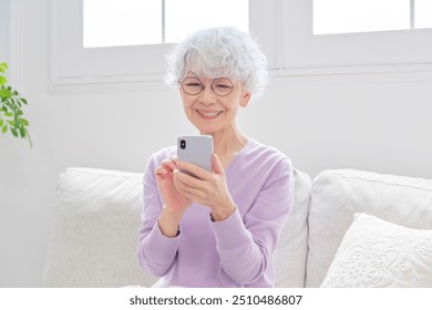 Asian senior woman using the smartphone in the living room - Powered by Shutterstock