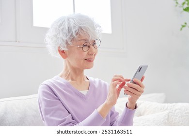 Asian senior woman using the smartphone in the living room - Powered by Shutterstock