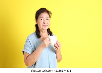 The Asian Senior Woman Wearing Light Blue Shirt Standing On The Yellow Background.