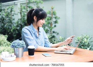 Asian Shopper Girl Buying Online With A Laptop And Credit Card Sitting In Garden At Home.