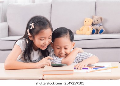 Asian siblings laughing together while using digital tablet. Young boy and girl sitting at table watch cartoons at home. Bright indoor setting, joyful expression, sibling bonding, technology use. - Powered by Shutterstock