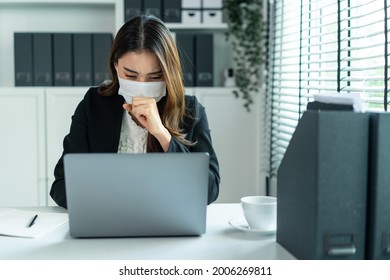 Asian Sick Businesswoman In Formal Wear Facemask And Work At Workplace. Attractive Female Employee Office Worker Coughing While Use Laptop Computer To Discuss For Company Plan During Covid19 Pandemic