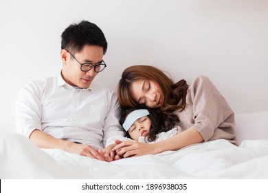 Asian Sick Girl Sleeping On The Bed With Fever Gel Pack On Her Forehead. Father And Mother Take Care Of Their Little Young Daughter Who Got A Fever From Flu Virus. Sick Little Kid Laying On The Bed.