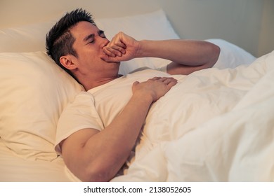 Asian Sick Handsome Male In Pajamas Sleep In The Dark Night In Bedroom. Attractive Young Man Feel Bad With Fever Illness And Coughing While Lying Down On Bed In House. Health Care And Medical Concept.