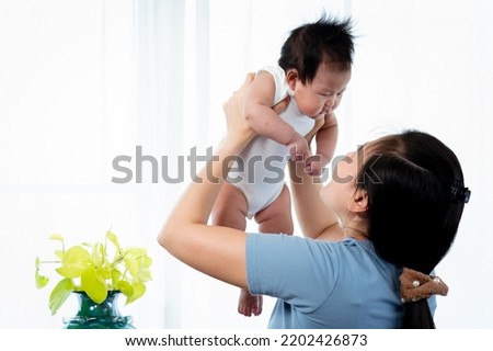 Asian single mom, holding up his daughter, The mother held daughter up to tease her, and she kissed her nose on cheek, The daughter looked at her mother, and smiled at joyfully.