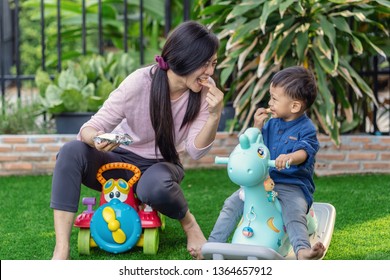 Asian Single Mom With Son Are Playing With Toy And Eating Together When Living In Front Lawn Of Modern House For Self Learning Or Home School, Family And Single Mom Concept, Selective Focus