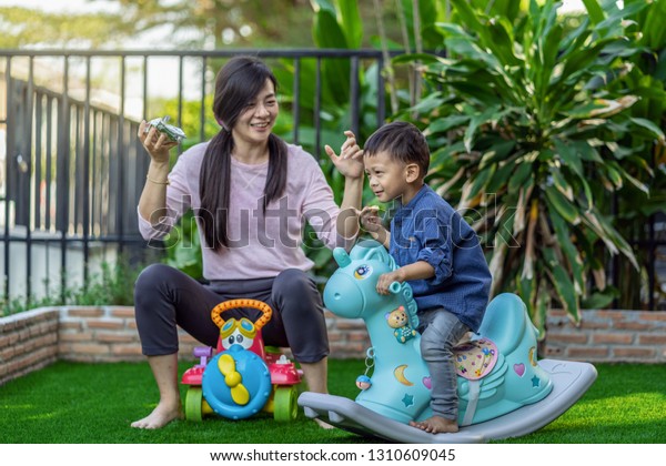 Asian single mom with son are playing with toy and\
eating together when living in Front lawn of modern house for Self\
learning or home school, Family and single mom concept, selective\
focus