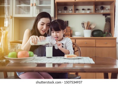 Asian single mother helping little daughter pouring milk to glass with breakfast together at home kitchen in the morning,World Milk Day - Powered by Shutterstock