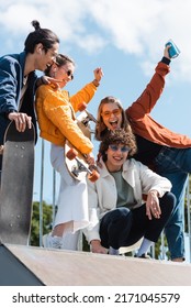 Asian Skater Pointing At Overjoyed Friends Screaming With Raised Hands Outdoors