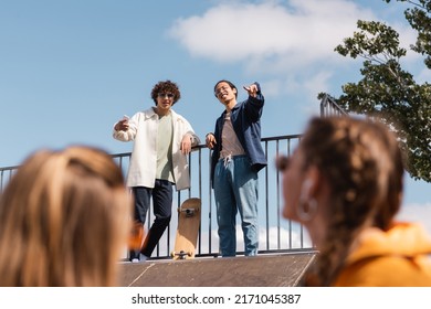 Asian Skater Standing On Skate Ramp And Pointing With Finger At Blurred Friends