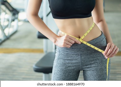 asian slim fitness woman working out in gym with waist measurement, portrait of fitness woman in gym posing for lean body and thin waistline, successful diet and healthy lifestyle concept