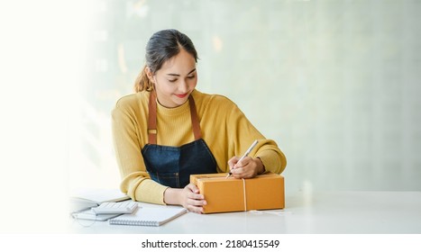 Asian Small business entrepreneur SME writing address on cardboard box at workplace small business entrepreneur SME , working with box at home.  - Shutterstock ID 2180415549
