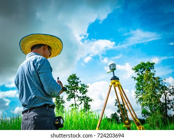 Asian Smart Engineer Or Surveyor Working On Controller Screen For Surveying Land In Rice Field, Thailand. GPS Surveying Instrument. GPS Equipment. Land Survey For Map. People Work In Good Environment.