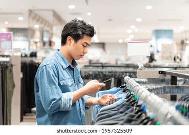 Asian Smart Man Using His Phone Is Picking Up Clothes In The Clothing Store In The Shopping Mall,