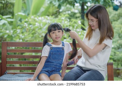 Asian Smiling Child Schoolgirl With Long Dark Hair And Her Mom In The Morning, Happy Family Beautiful Mother Woman Brushing Her Daughter Hair While Sitting Outdoor At Home, Hairstyle Care Concept