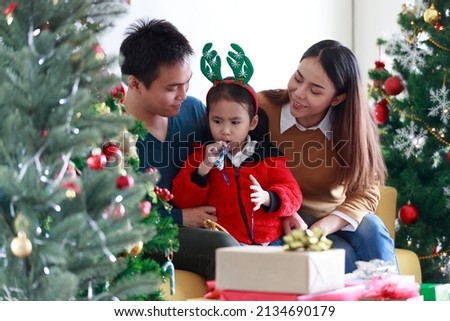 Asian smiling daughter happy teased the father and mother. My dad, mom and baby in Santa hats sitting on a couch at home near the Christmas tree. Concept Tease Love Cozy Smile lovely