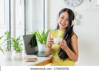 Asian Smiling Girl Student Wear Wireless Headphone Study Online With Skype Teacher In A Coffee Shop, Woman Learn Language Listen Lecture Look At The Camera Sit In Cafe, Distant Education, New Normal