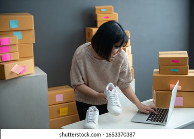 Asian Smiling Girl Using Smartphone To Shoot White Sneaker Posted For Sale On The Internet.startup Small Business Owner Working With Tablet At Workplace.happy Owner & Seller Check Product To Customer