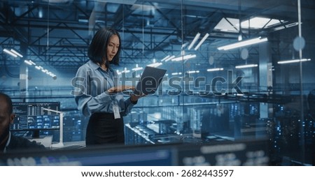 Asian Software Developer Analyze System Performance Metrics on a Laptop Inside a Modern Data Center. Young Female Manager Ensuring Efficient Operations for Critical Infrastructure