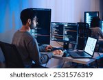 Asian software developers working on multiple screens displaying code and application diagrams at night in modern office