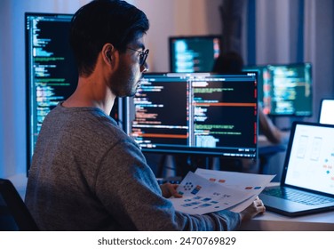 Asian software developers working on multiple screens displaying code and application diagrams at night in modern office