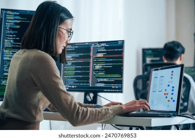 Asian software developers working on multiple screens displaying code and application diagrams in a modern office - Powered by Shutterstock