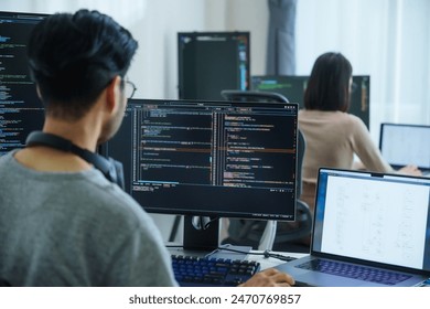 Asian software developers working on multiple screens displaying code and application diagrams in a modern office