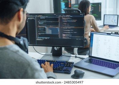 Asian software developers working on multiple screens displaying code and application diagrams in a modern office