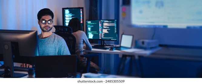 Asian software developers working on multiple screens displaying code and application diagrams at night in modern office - Powered by Shutterstock