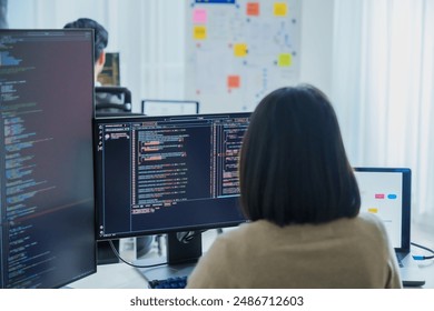 Asian software developers working on multiple screens displaying code and application diagrams in a modern office