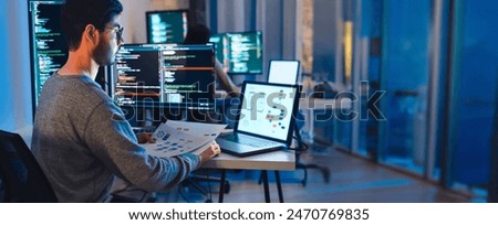 Asian software developers working on multiple screens displaying code and application diagrams at night in modern office