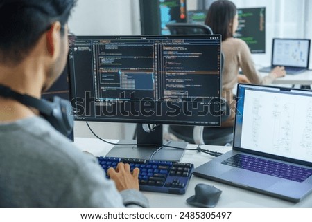 Asian software developers working on multiple screens displaying code and application diagrams in a modern office