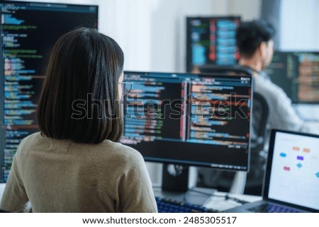 Asian software developers working on multiple screens displaying code and application diagrams in a modern office