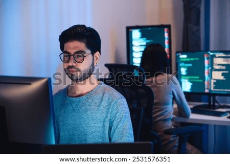 Asian software developers working on multiple screens displaying code and application diagrams at night in modern office